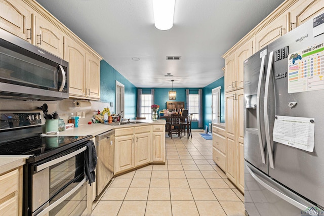 kitchen featuring decorative light fixtures, light brown cabinets, light tile patterned floors, and stainless steel appliances