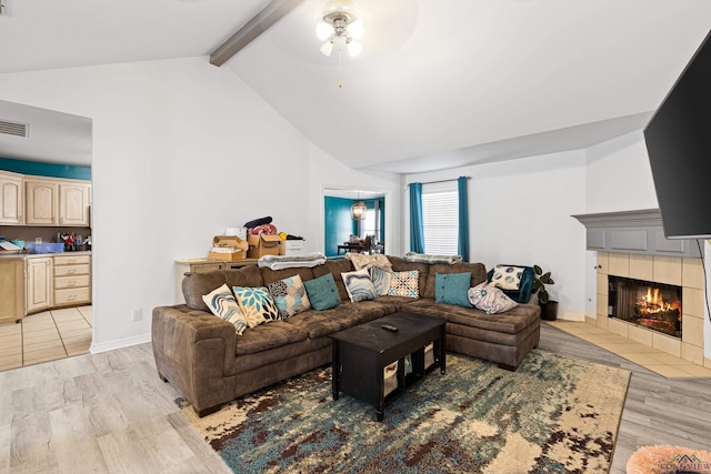 living room featuring lofted ceiling with beams, ceiling fan, light wood-type flooring, and a tile fireplace