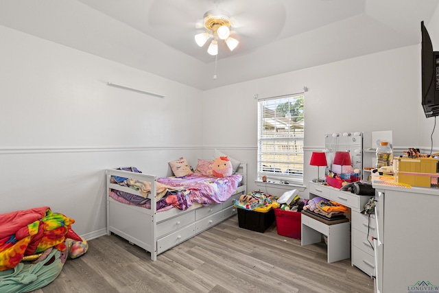 bedroom featuring ceiling fan, light hardwood / wood-style floors, and a tray ceiling