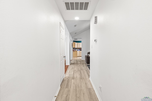 hallway with light wood-type flooring and vaulted ceiling