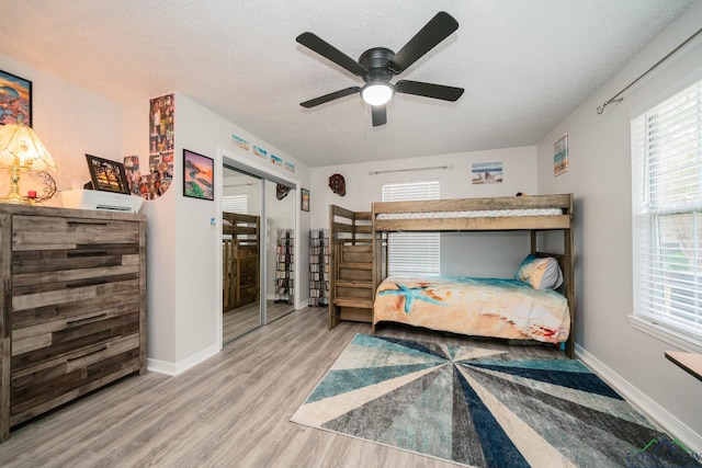 bedroom with ceiling fan, light hardwood / wood-style flooring, a textured ceiling, multiple windows, and a closet