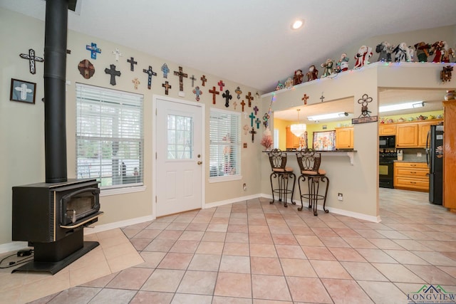 tiled entrance foyer with a notable chandelier, a wood stove, and vaulted ceiling