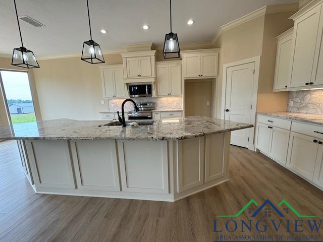 kitchen featuring sink, tasteful backsplash, decorative light fixtures, a kitchen island with sink, and appliances with stainless steel finishes