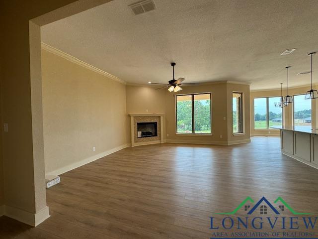 unfurnished living room featuring a wealth of natural light, dark hardwood / wood-style floors, ceiling fan with notable chandelier, and ornamental molding