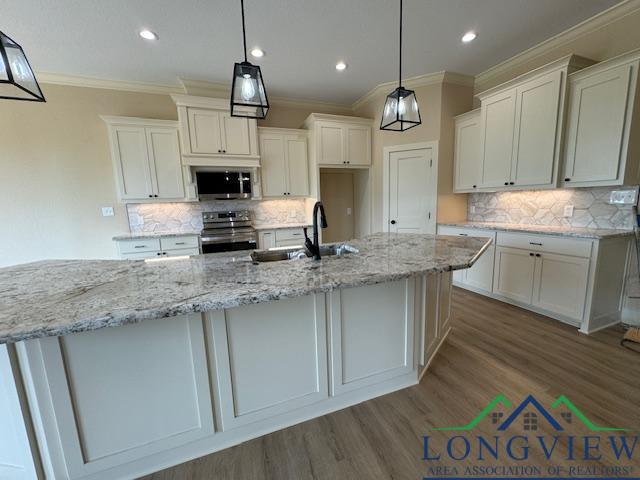 kitchen with white cabinets, stainless steel appliances, a center island with sink, and sink