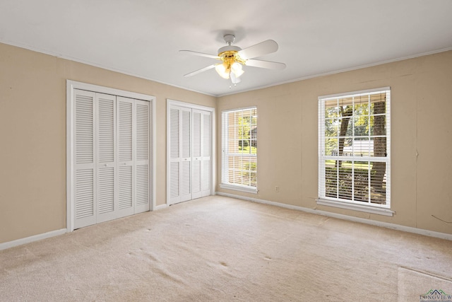 unfurnished bedroom with ceiling fan, multiple windows, and two closets