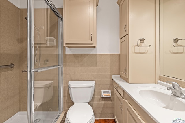 bathroom with vanity, a shower with shower door, tile walls, and toilet