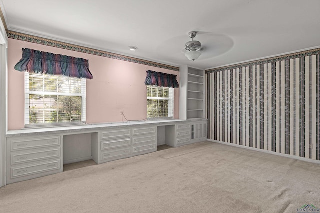 unfurnished office featuring ceiling fan, light colored carpet, and built in desk