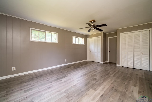 unfurnished bedroom with ceiling fan, wood-type flooring, crown molding, and multiple closets