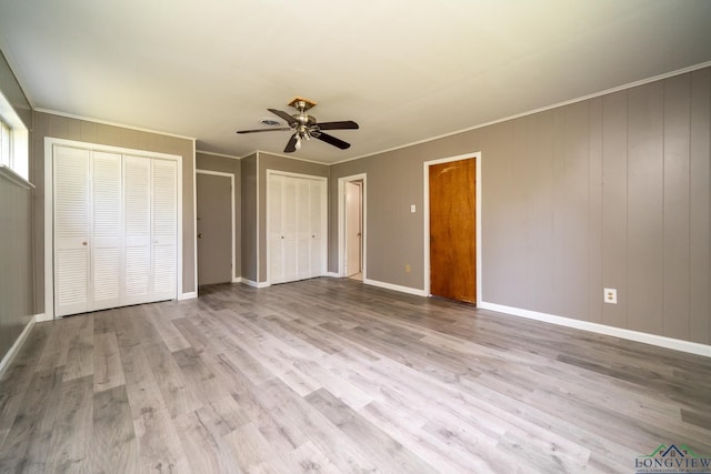 unfurnished bedroom featuring ornamental molding, light hardwood / wood-style floors, ceiling fan, and multiple closets