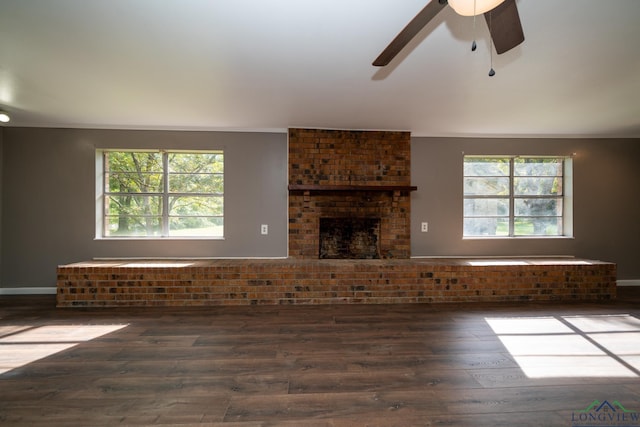 unfurnished living room with ceiling fan, a fireplace, dark wood-type flooring, and a wealth of natural light