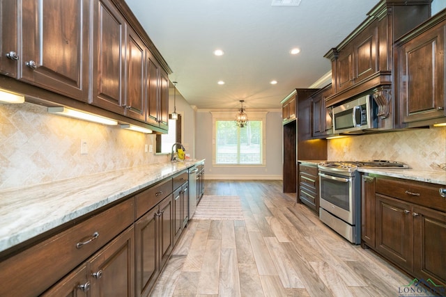 kitchen with sink, backsplash, light hardwood / wood-style floors, decorative light fixtures, and appliances with stainless steel finishes