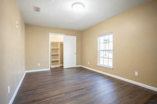 unfurnished bedroom featuring a walk in closet, dark hardwood / wood-style flooring, and a closet