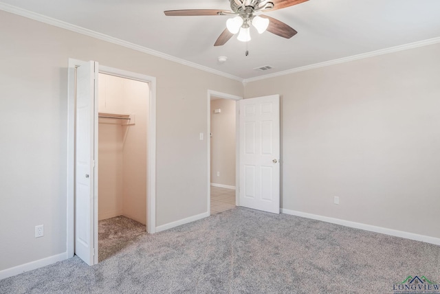 unfurnished bedroom featuring a closet, light colored carpet, crown molding, ceiling fan, and a spacious closet