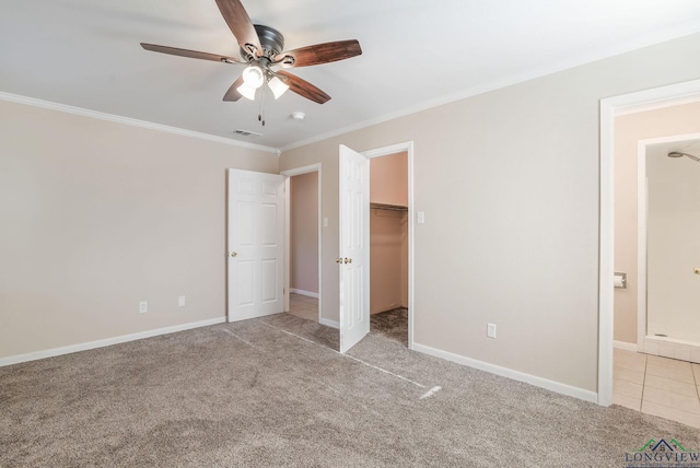 unfurnished bedroom with ceiling fan, a walk in closet, ornamental molding, and light colored carpet