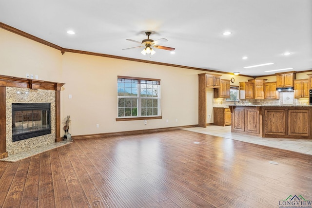 unfurnished living room featuring ornamental molding, a high end fireplace, light wood-style floors, baseboards, and ceiling fan