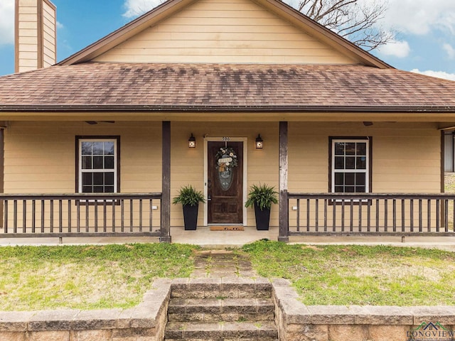 view of front facade with covered porch, roof with shingles, and a chimney