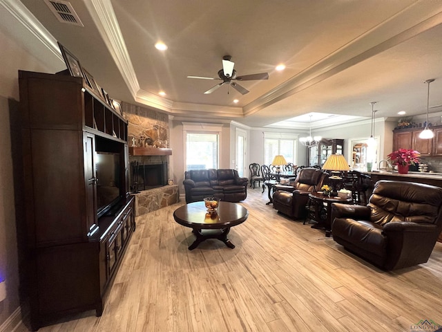 living room featuring ceiling fan with notable chandelier, a raised ceiling, light wood-type flooring, a fireplace, and ornamental molding