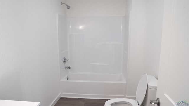 bathroom with washtub / shower combination, wood-type flooring, and toilet