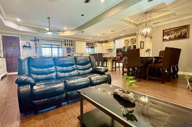 living room featuring hardwood / wood-style floors, ceiling fan with notable chandelier, a raised ceiling, and crown molding