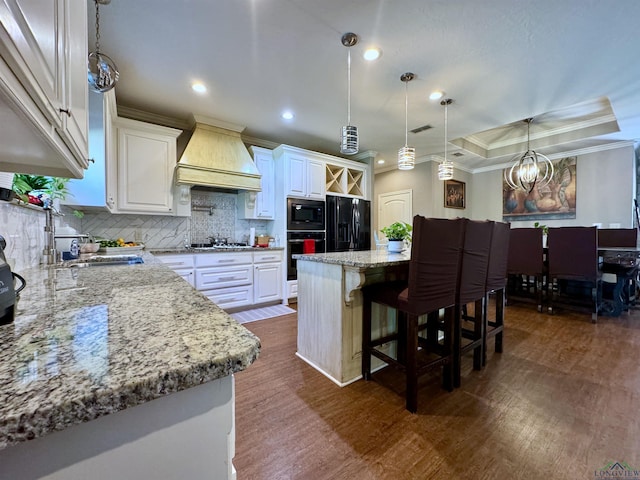 kitchen with white cabinetry, decorative light fixtures, a kitchen island, black appliances, and custom range hood