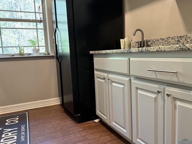 interior space featuring black fridge, light stone countertops, dark hardwood / wood-style flooring, and white cabinets