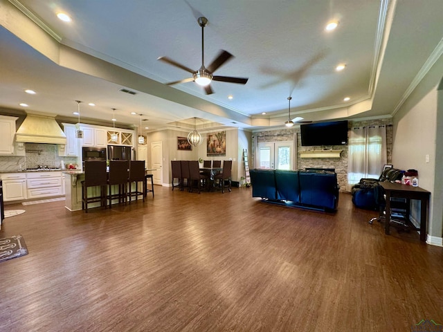 living room featuring dark wood-type flooring, a raised ceiling, crown molding, ceiling fan, and a fireplace