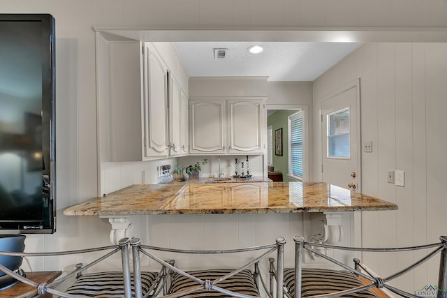1303 Le Duke Blvd, Longview, TX 75601 - kitchen with light stone countertops, a kitchen breakfast bar, a peninsula, white cabinetry, and a textured ceiling