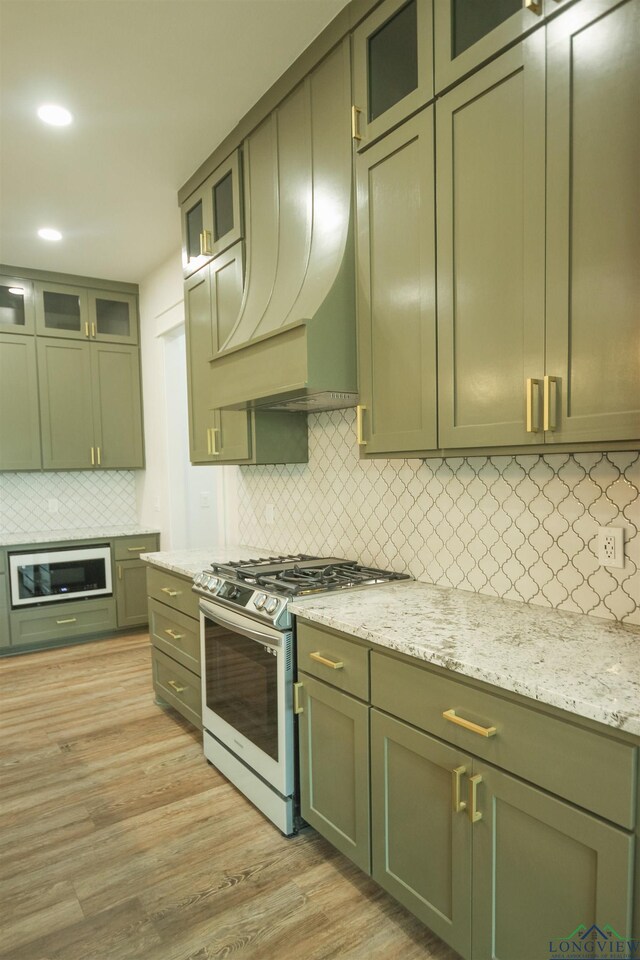 kitchen with stainless steel range with gas cooktop, sink, hanging light fixtures, a kitchen island with sink, and light stone counters