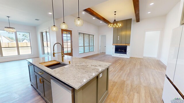kitchen featuring sink, light stone counters, decorative light fixtures, a kitchen island with sink, and backsplash
