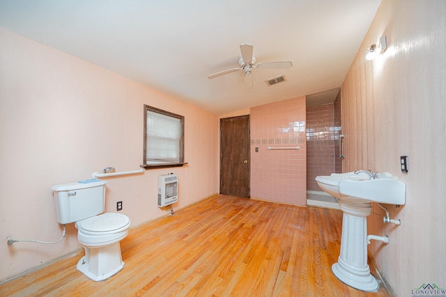 bathroom with heating unit, ceiling fan, tiled shower, hardwood / wood-style flooring, and toilet