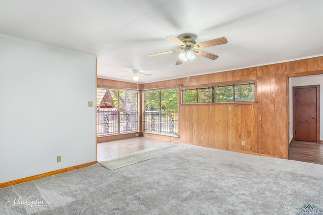 empty room with ceiling fan, ornamental molding, wooden walls, and carpet