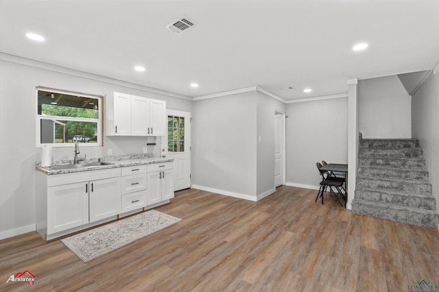 kitchen with a sink, visible vents, white cabinets, baseboards, and light wood-style floors