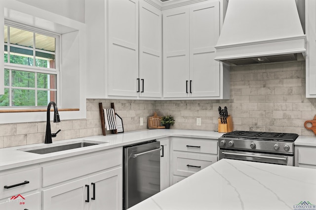 kitchen with a sink, tasteful backsplash, custom exhaust hood, white cabinets, and appliances with stainless steel finishes