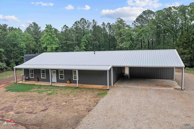 view of front of home featuring metal roof, a porch, a view of trees, and driveway