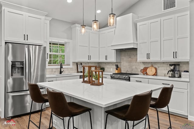 kitchen featuring visible vents, a sink, a kitchen bar, premium range hood, and stainless steel appliances