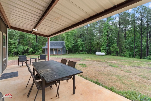 view of patio featuring a wooded view, an outbuilding, outdoor dining space, and a shed