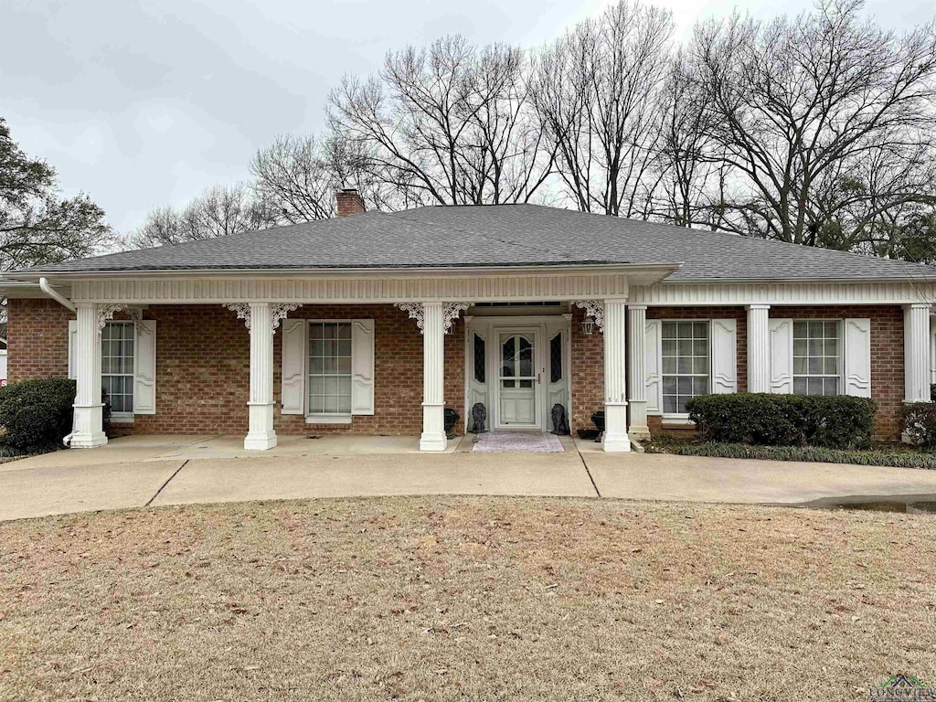 view of front of home with roof with shingles, brick siding, a chimney, and a porch