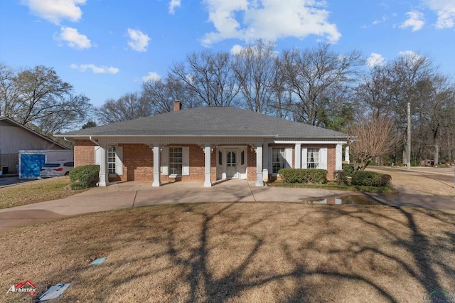 view of front of house with a porch, brick siding, a chimney, and a front yard