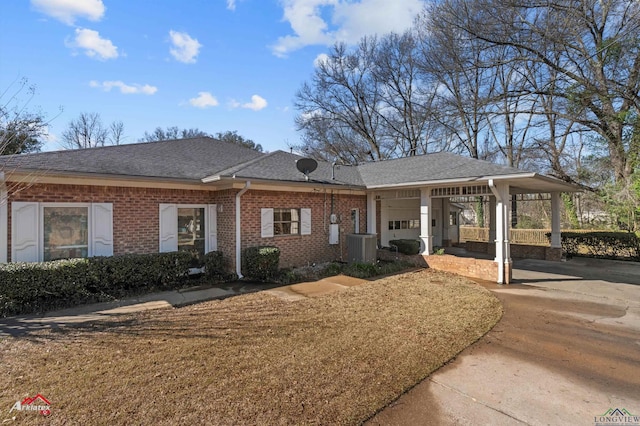 view of front of property featuring cooling unit, roof with shingles, driveway, brick siding, and an attached carport