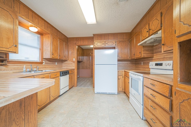 kitchen featuring white appliances, wooden walls, sink, and a textured ceiling