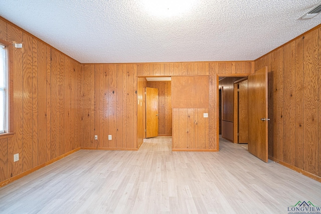 empty room featuring a textured ceiling, light wood-type flooring, and wood walls