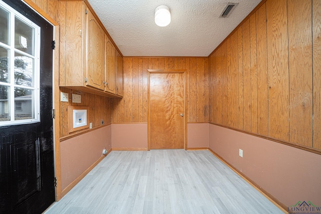 washroom with wooden walls, cabinets, washer hookup, light hardwood / wood-style floors, and a textured ceiling