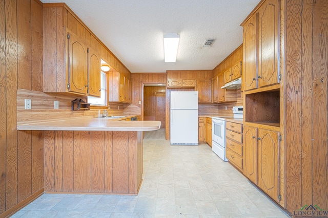 kitchen with wood walls, sink, white appliances, kitchen peninsula, and a textured ceiling