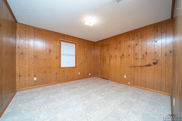 unfurnished room featuring a textured ceiling and wood walls