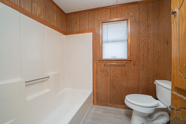 bathroom featuring toilet, wood-type flooring, a textured ceiling, wooden walls, and a bath