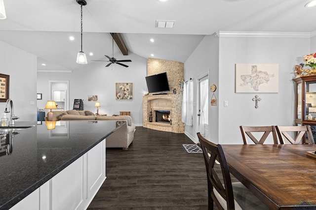 dining space featuring ceiling fan, sink, dark wood-type flooring, vaulted ceiling with beams, and a fireplace