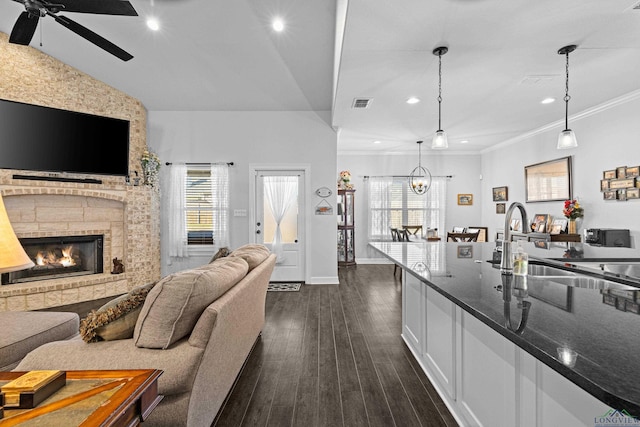 kitchen with dark stone counters, dark wood-type flooring, decorative light fixtures, white cabinetry, and a stone fireplace