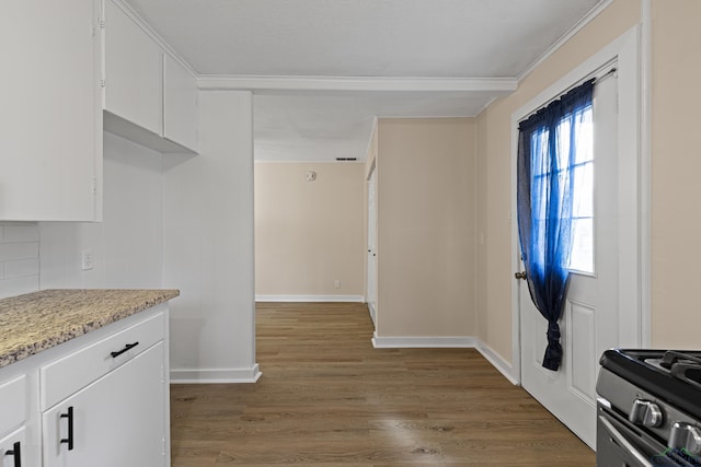 kitchen with hardwood / wood-style floors, ornamental molding, stainless steel range with gas stovetop, and white cabinetry