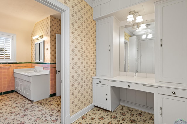 bathroom with wainscoting, vanity, tile walls, and wallpapered walls